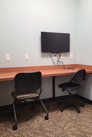 Small room with a desk, 2 chairs and a wall mounted screen